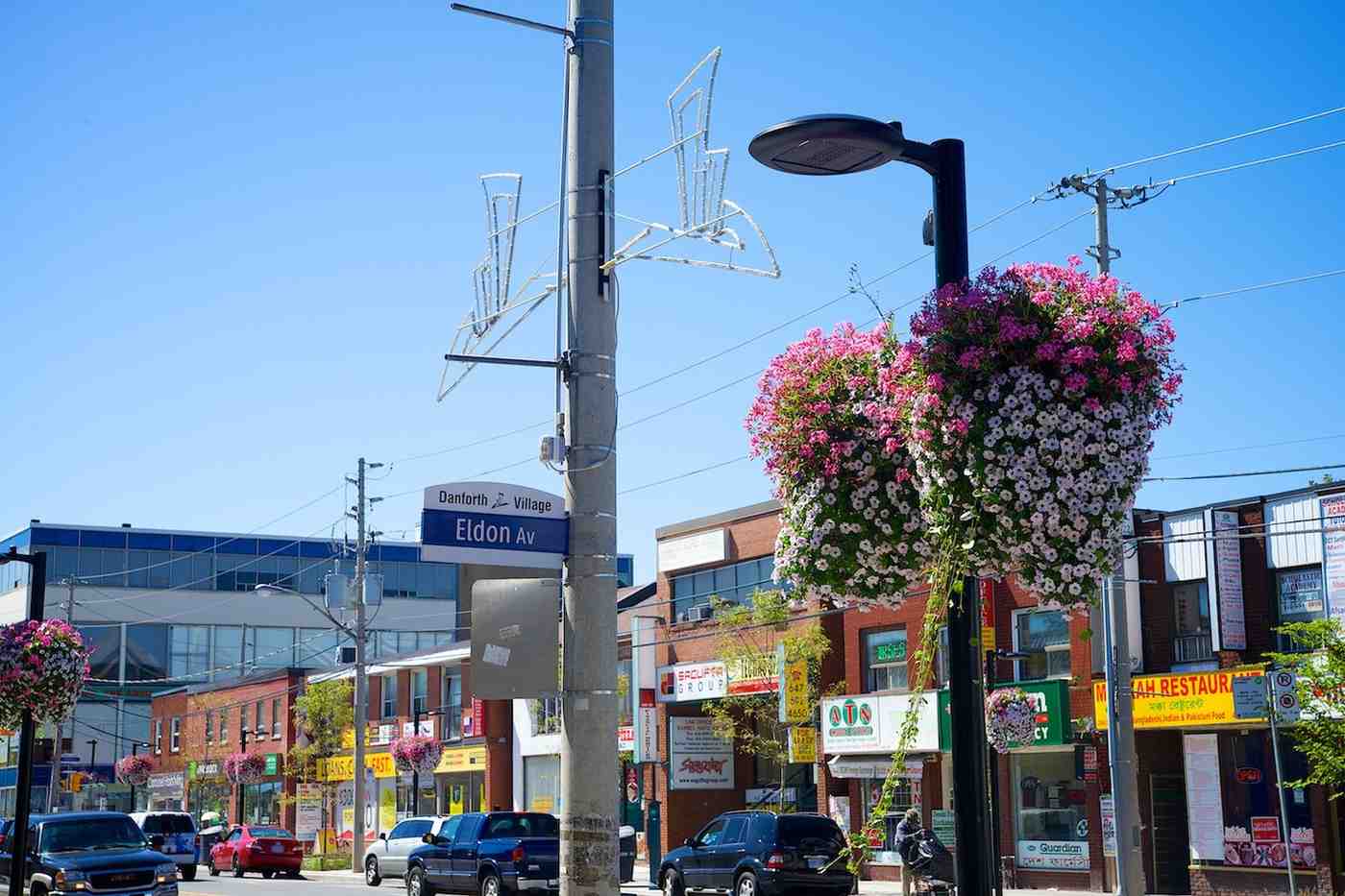 Municipal floral hoops supporting hanging flower baskets on a street pole in a Toronto BIA streetscape.